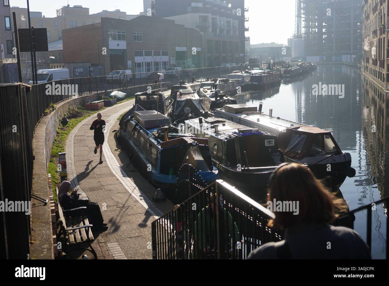 La vista del sentiero sul Regent's Canal al sole del mattino presto della primavera. Le barche della casa costeggiano il canale con i lavori di costruzione alle spalle. Foto Stock