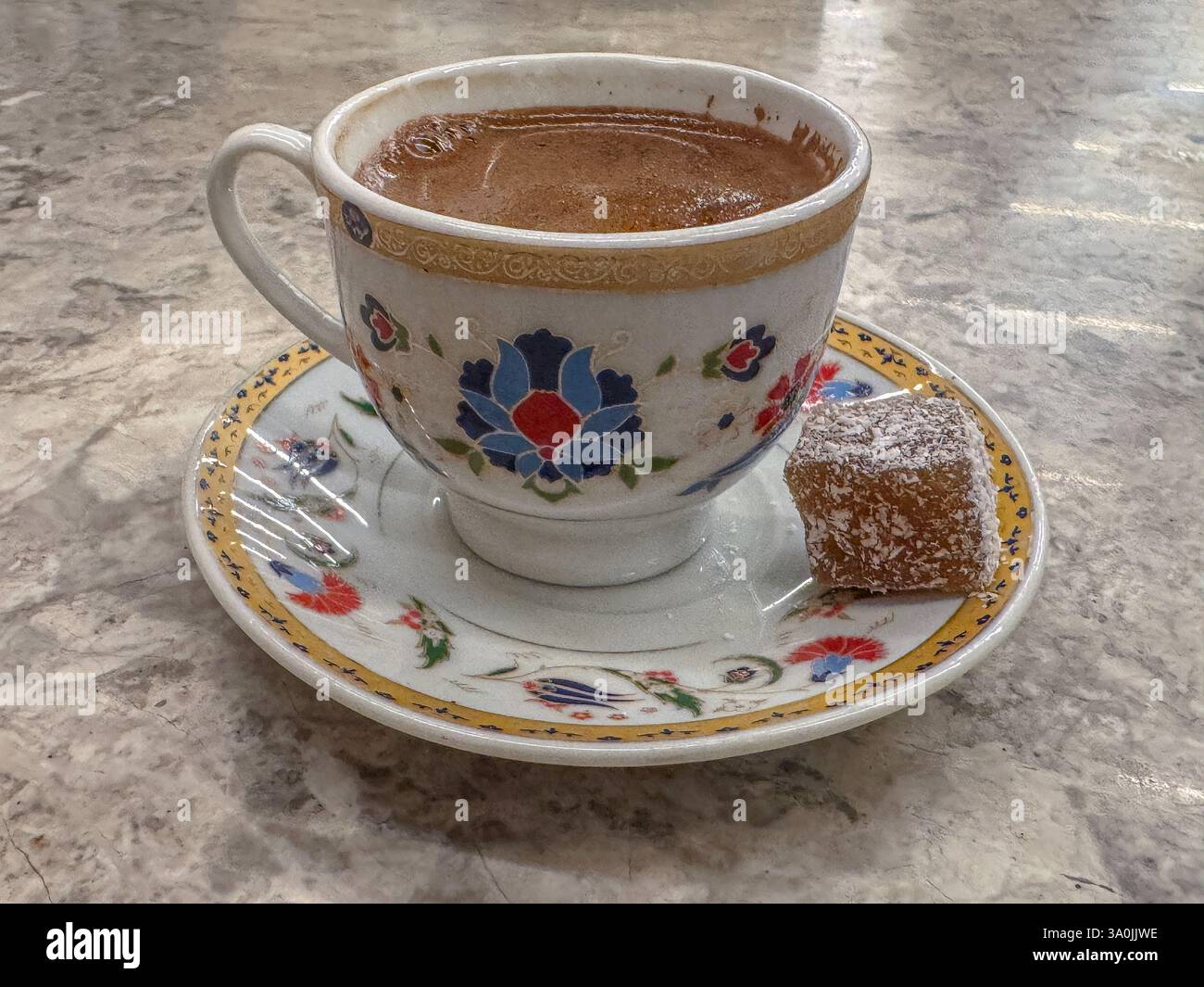 Una tazza floreale splendidamente dipinta contenente il tradizionale caffè turco, accompagnato da un pezzo di delizia turca servita su una dettagliata salsa decorativa Foto Stock
