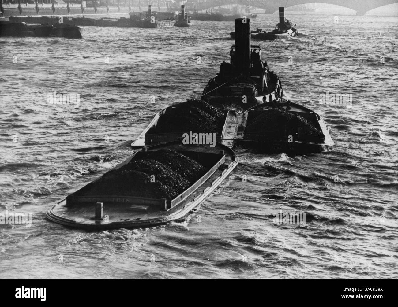 Heavy Passage sul Tamigi durante il Gale -- Un robusto rimorchiatore, una serie di chiatte di carbone pesantemente cariche al seguito, combatte la sua strada sul Tamigi al largo di Westminister durante le galee che hanno colpito Londra. 23 novembre 1938. Foto Stock