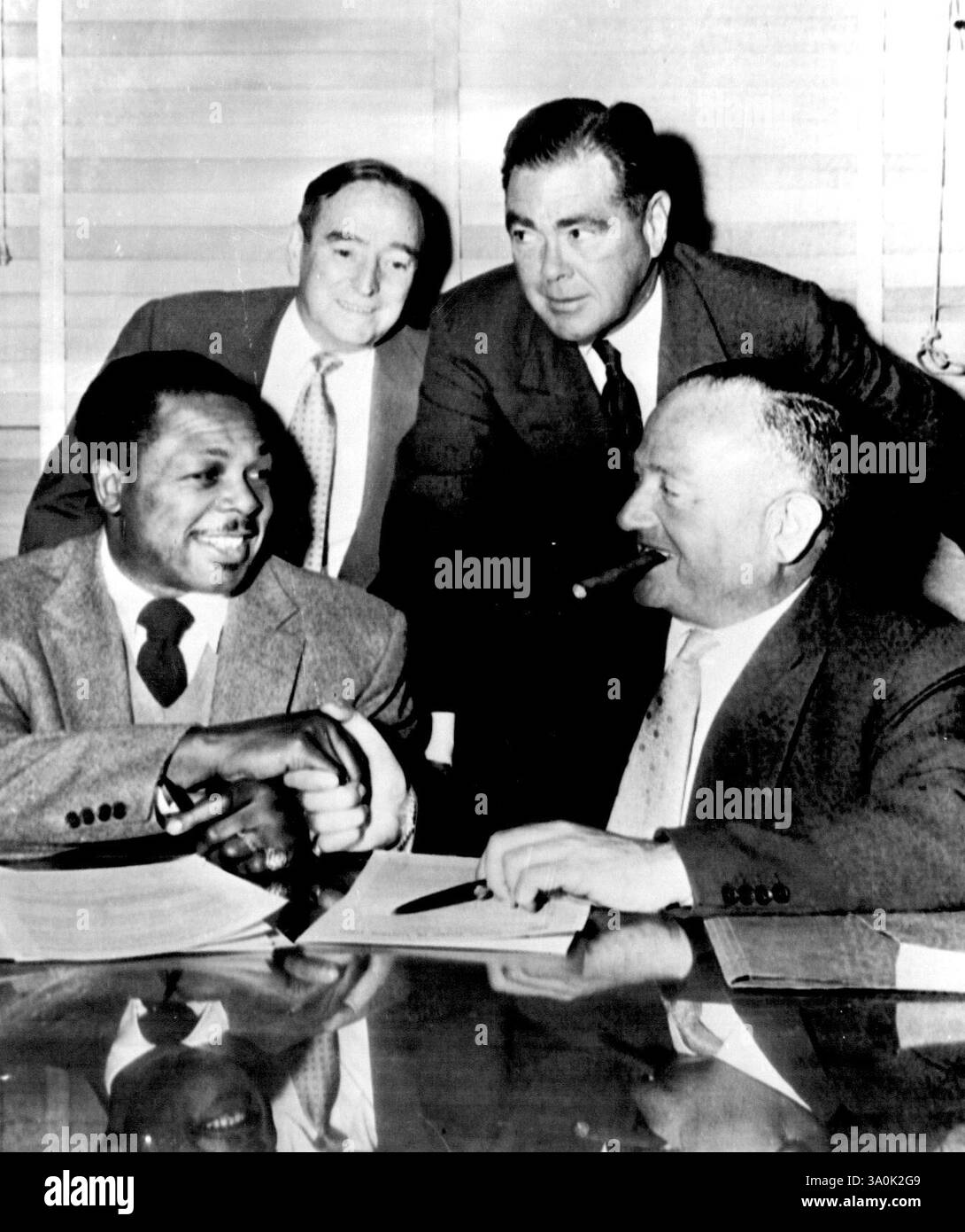 Moore's Mitt on London Bout - il campione dei pesi mediomassimi Archie Moore, a sinistra, stringe la mano a Jack Solomons, promotore di boxe britannico, dopo aver cantato il contratto oggi top difende il suo titolo contro Yolando Pompey, di Trinidad, a Londra il 10 gennaio. Sul retro, nell'ufficio del Madison Square Garden dell'International Boxing Club, si trovano Charley Johnston, a sinistra, il manager di Moore, e James D. Norris, presidente dell'I.B.C. Bout, che si terranno all'Earl's Court Arena. Pompeo, 26 anni, US quarto classificato 175-pound contender. 1° novembre 1955. (Foto di AP Wirephoto). Foto Stock