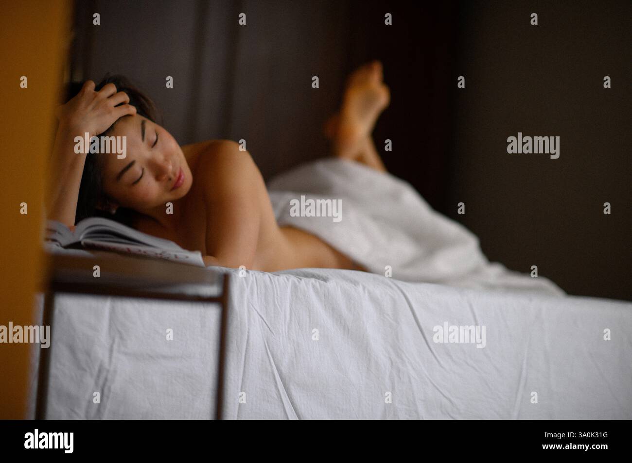 Bella donna asiatica sdraiata a letto che legge un libro. Momenti di relax che simboleggiano il riposo, il comfort, il tempo libero e il tempo libero. Foto Stock