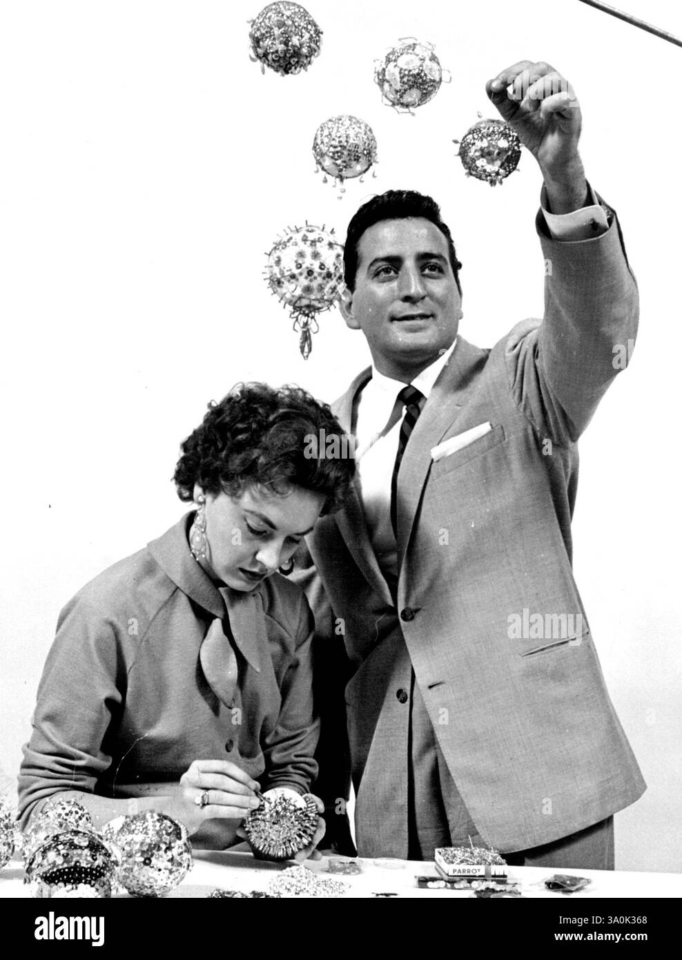 Gioielli finti nel glitter natalizio. Sandy Bennett, moglie del cantante Tony Bennett, mostra come realizza i suoi ornamenti per alberi di Natale con pezzi di glitter, spille e polistirolo dal fiorista (sotto) : Shape the White Styrofoam into balls. Quindi, con le spille dritte, incollare pezzi di gioielli spazzatura (paillettes, perle, perline, orecchini rotti) nelle palle. Un detergente per tubi fissato a un'estremità lo rende pronto per essere appeso all'albero. Decora un albero di Natale all'aperto con strisce di nastro fluorescente. Si illumineranno ogni volta che i fari delle automobili si illuminano. 5 agosto 1955. Foto Stock
