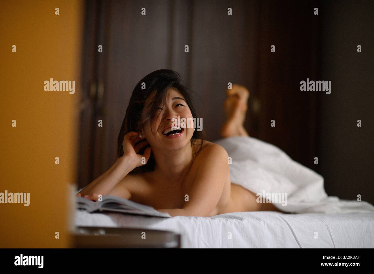 Bella donna asiatica sdraiata a letto che legge un libro. Momenti di relax che simboleggiano il riposo, il comfort, il tempo libero e il tempo libero. Foto Stock