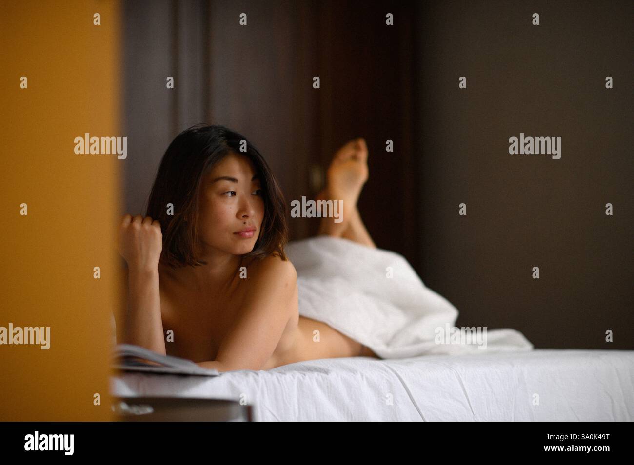 Bella donna asiatica sdraiata a letto che legge un libro. Momenti di relax che simboleggiano il riposo, il comfort, il tempo libero e il tempo libero. Foto Stock