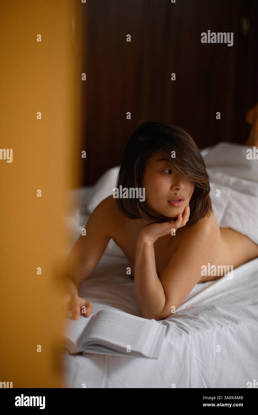 Bella donna asiatica sdraiata a letto che legge un libro. Momenti di relax che simboleggiano il riposo, il comfort, il tempo libero e il tempo libero. Foto Stock