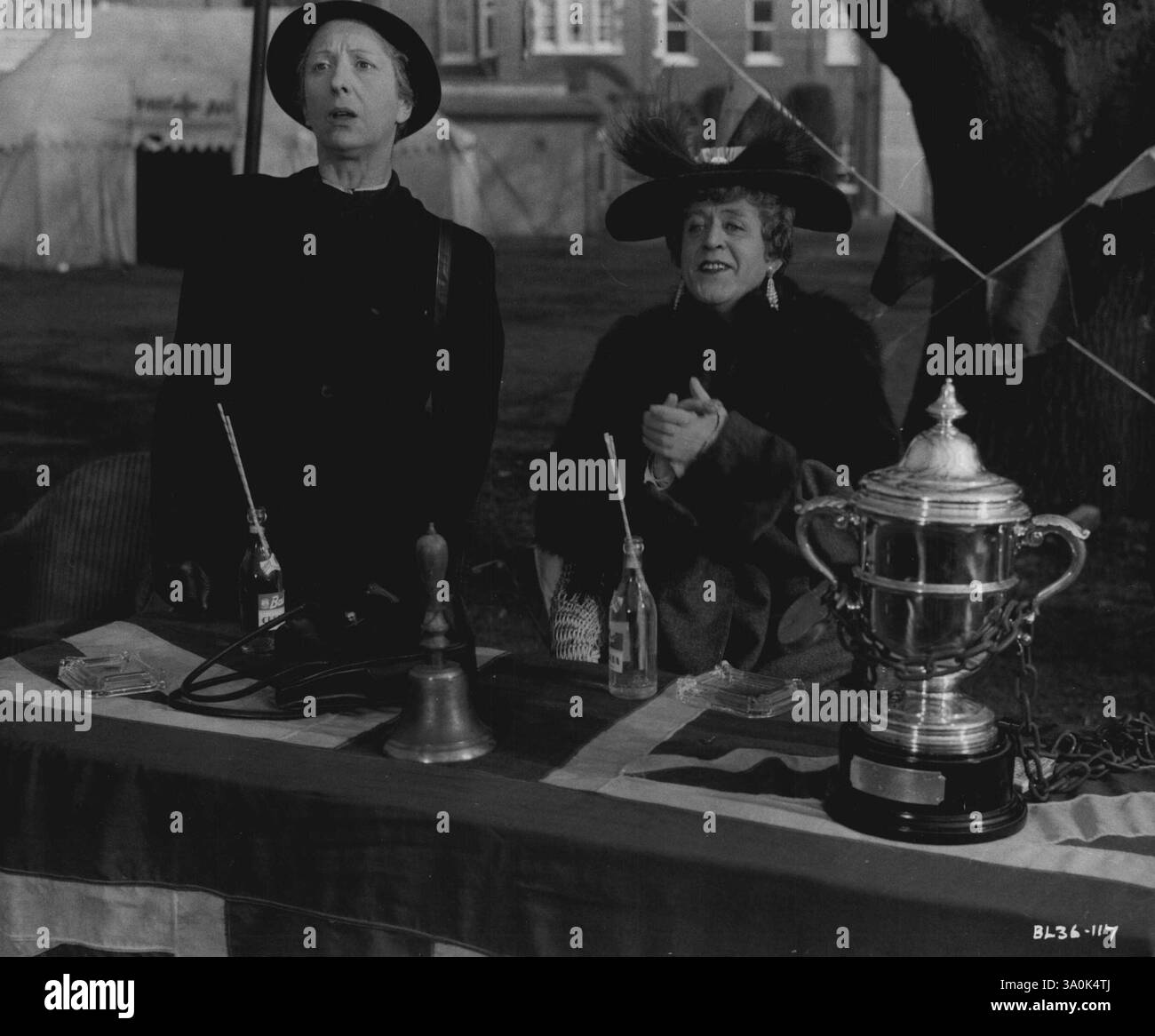 "Le Belles of St. Trinians": L'amante di Bilston, (Noel Hood) guarda con orrore i consueti avvenimenti sul campo di hockey di St. Trinians, mentre la direttrice Fritton (Alastair SIM) applaude. Quest'ultima, conoscendo le sue ragazze, e senza correre rischi, ha la tazza pesantemente incatenata al tavolo! È una produzione di launder-Gilliat per London Films, diretta da Frank Launder. Sceneggiatura di Frank Launder, Sidney Gilliat e Val Valentine, ispirata alle "terribili studentesse" di Ronald Searle. Interpretato da Alastair SIM (nel doppio ruolo di Headmistress Fritton e suo fratello bookmaker Clarence), con Joyce Grenfe Foto Stock