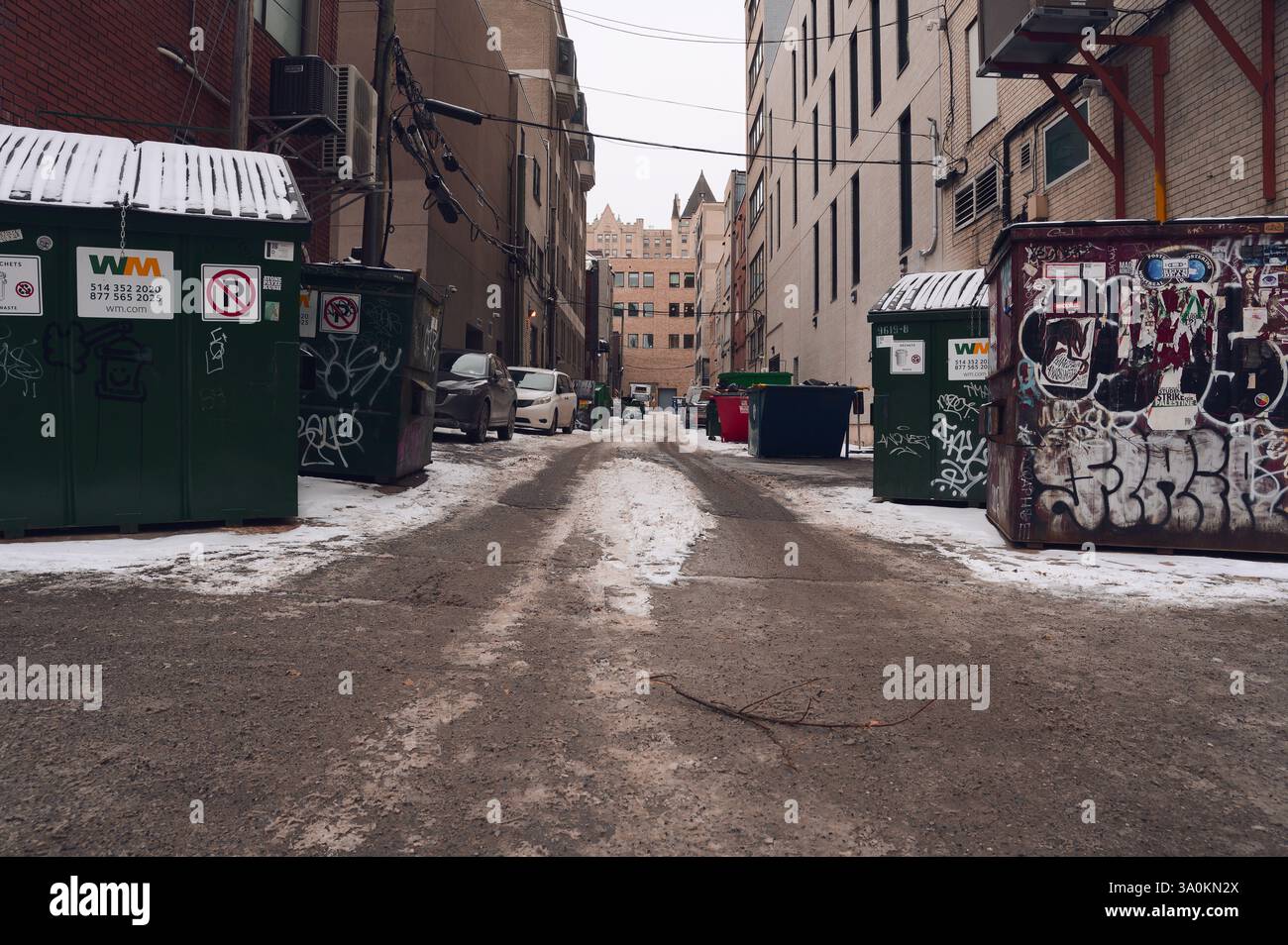 Vicolo del centro, deserto, che fiancheggia la neve sul marciapiede fiancheggiato da grandi container Foto Stock