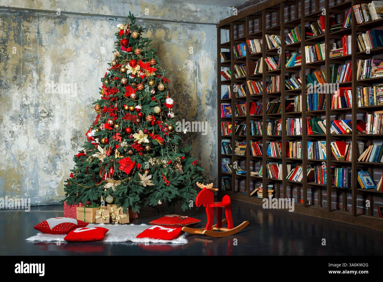 Un ambiente accogliente e festoso caratterizzato da un albero di Natale splendidamente decorato posto accanto a una grande libreria. L'albero è adornato con abbondanza di ornamenti Foto Stock