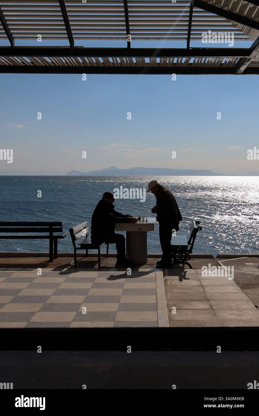 Atene, Grecia - 4 marzo 2025. Silhouette di due anziani che giocano a scacchi in riva al mare Foto Stock
