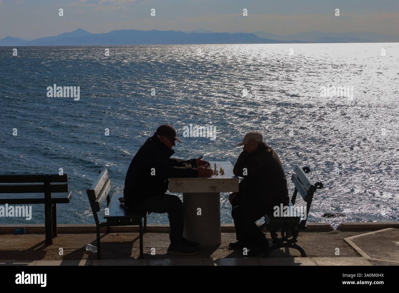 Atene, Grecia - 4 marzo 2025. Silhouette di due anziani che giocano a scacchi in riva al mare Foto Stock