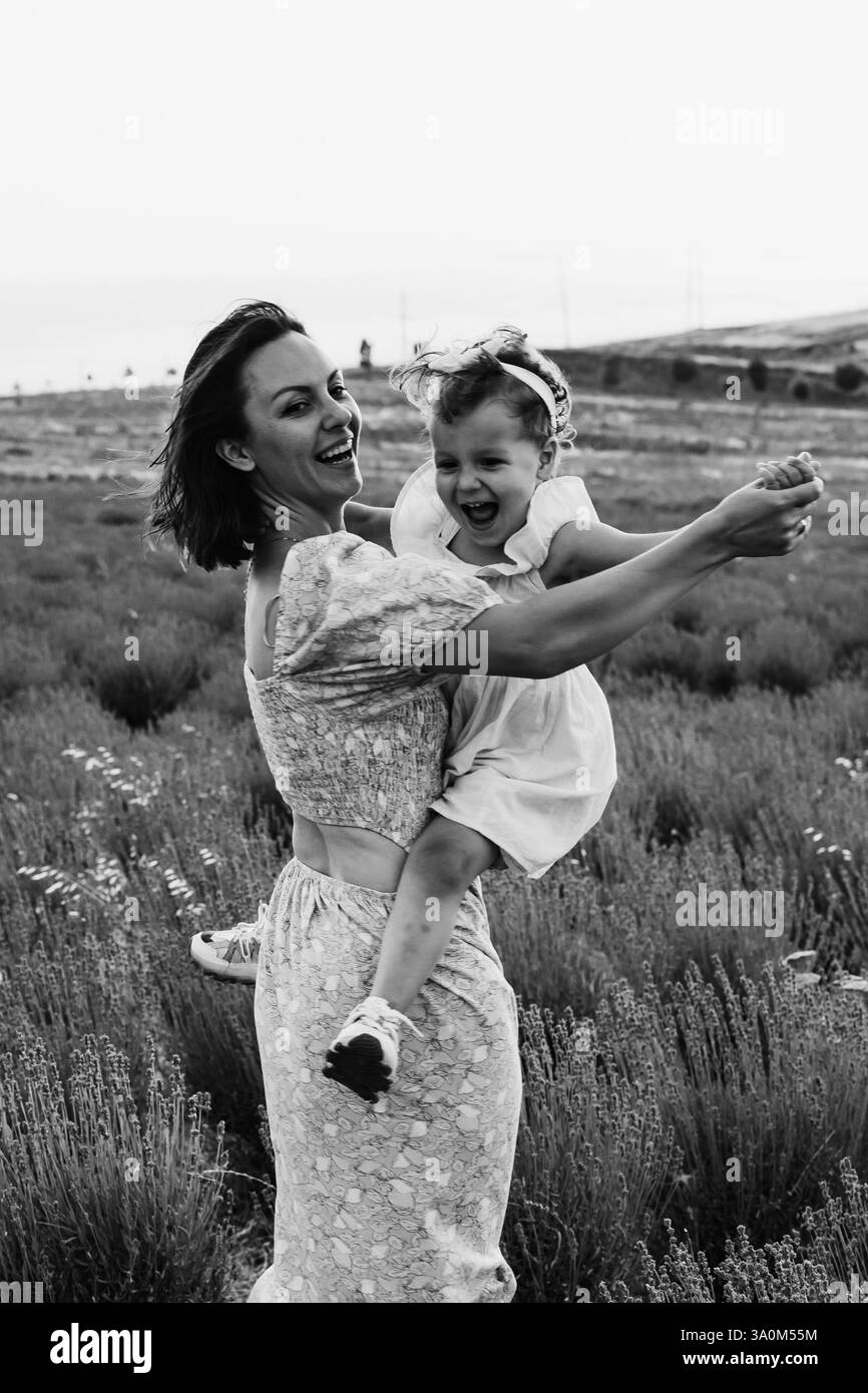Madre e figlia si godono un gioioso picnic, corrono nel parco, giocano vicino al lago e si divertono in un campo di lavanda. Abiti luminosi, estate Foto Stock