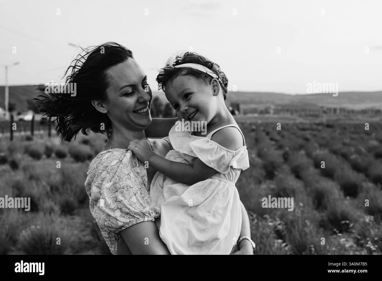 Madre e figlia si godono un gioioso picnic, corrono nel parco, giocano vicino al lago e si divertono in un campo di lavanda. Abiti luminosi, estate Foto Stock