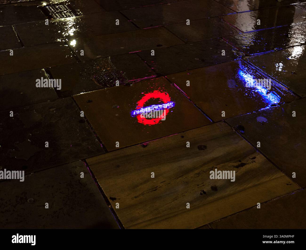 Logo della metropolitana di Londra / cerchio della metropolitana di Londra riflesso in una pozzanghera a Londra Kings Cross St Pancras Foto Stock