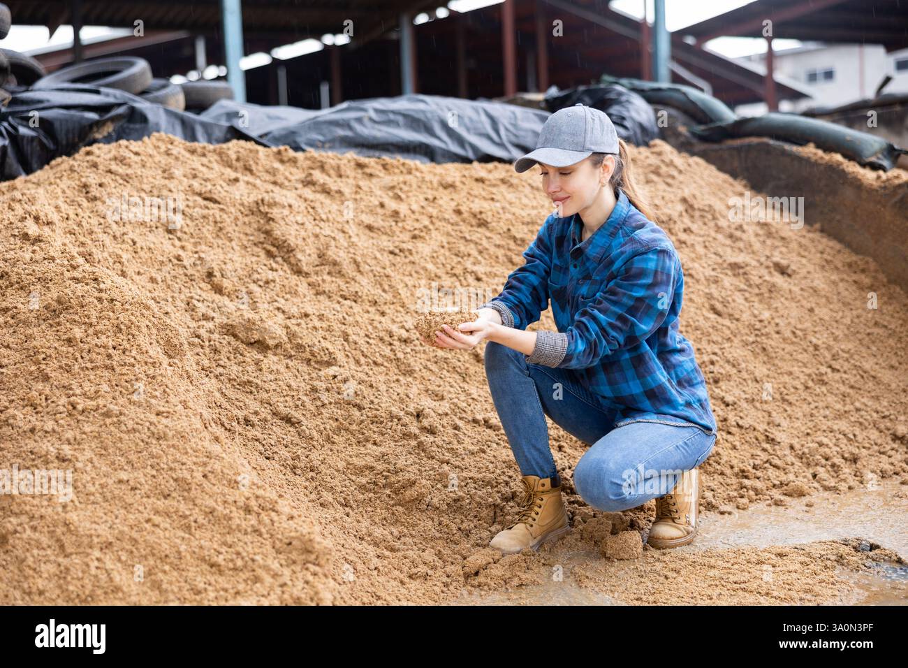 Agricoltore che controlla la qualità della bagasse di birra in un magazzino all'aperto Foto Stock