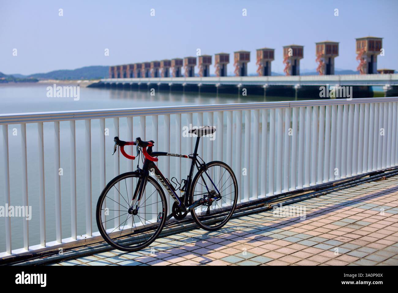 Gunsan, Corea del Sud - 28 maggio 2021: Una bicicletta da strada si appoggia contro una ringhiera presso la riva estuaria del fiume Geum, con le caratteristiche porte della diga Foto Stock