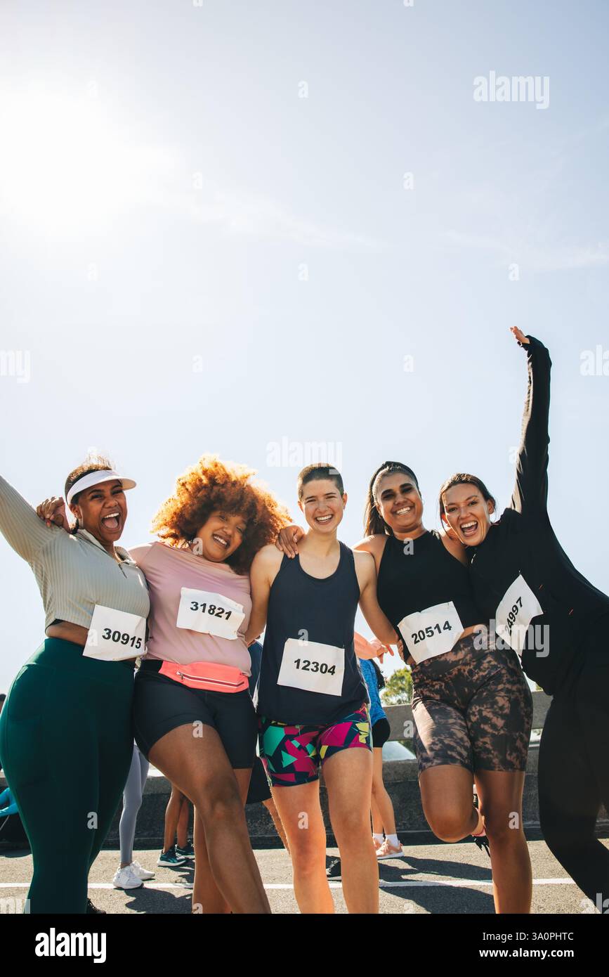 Un gruppo gioioso di cinque amiche festeggia il loro successo in una gara di 5 km. Posano insieme, irradiando felicità ed entusiasmo ed embo Foto Stock