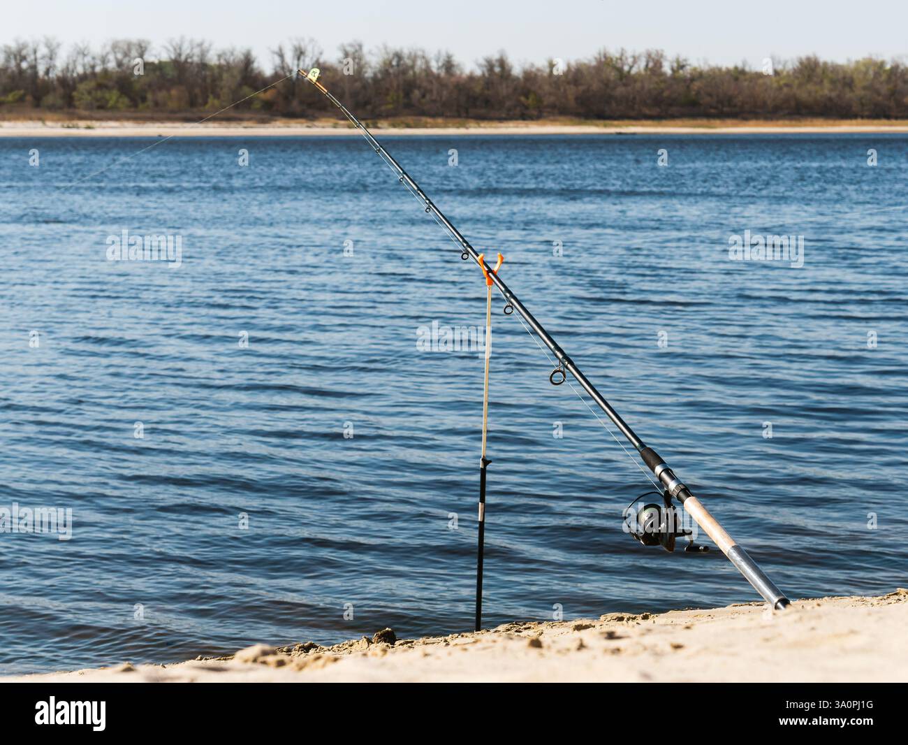 Canna da pesca con mulinello sulla riva sabbiosa di un ampio fiume. Foto Stock Canna da pesca con mulinello sulla riva sabbiosa di un ampio fiume. Foto Stock