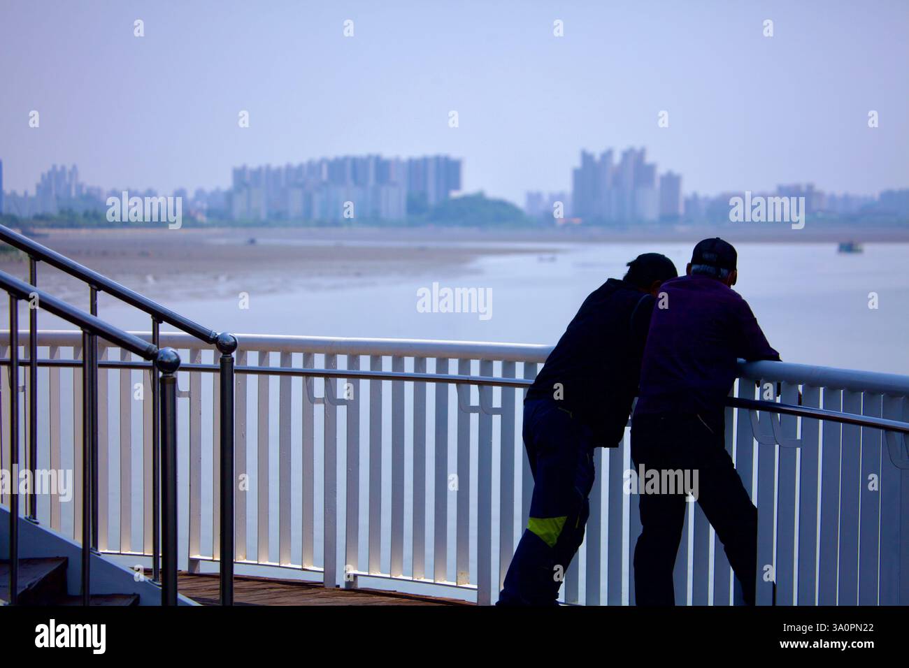 Gunsan, Corea del Sud - 28 maggio 2021: Due uomini si appoggiano contro una ringhiera, osservando l'estuario del fiume Geum, dove il fiume incontra il Mar giallo. Il di Foto Stock