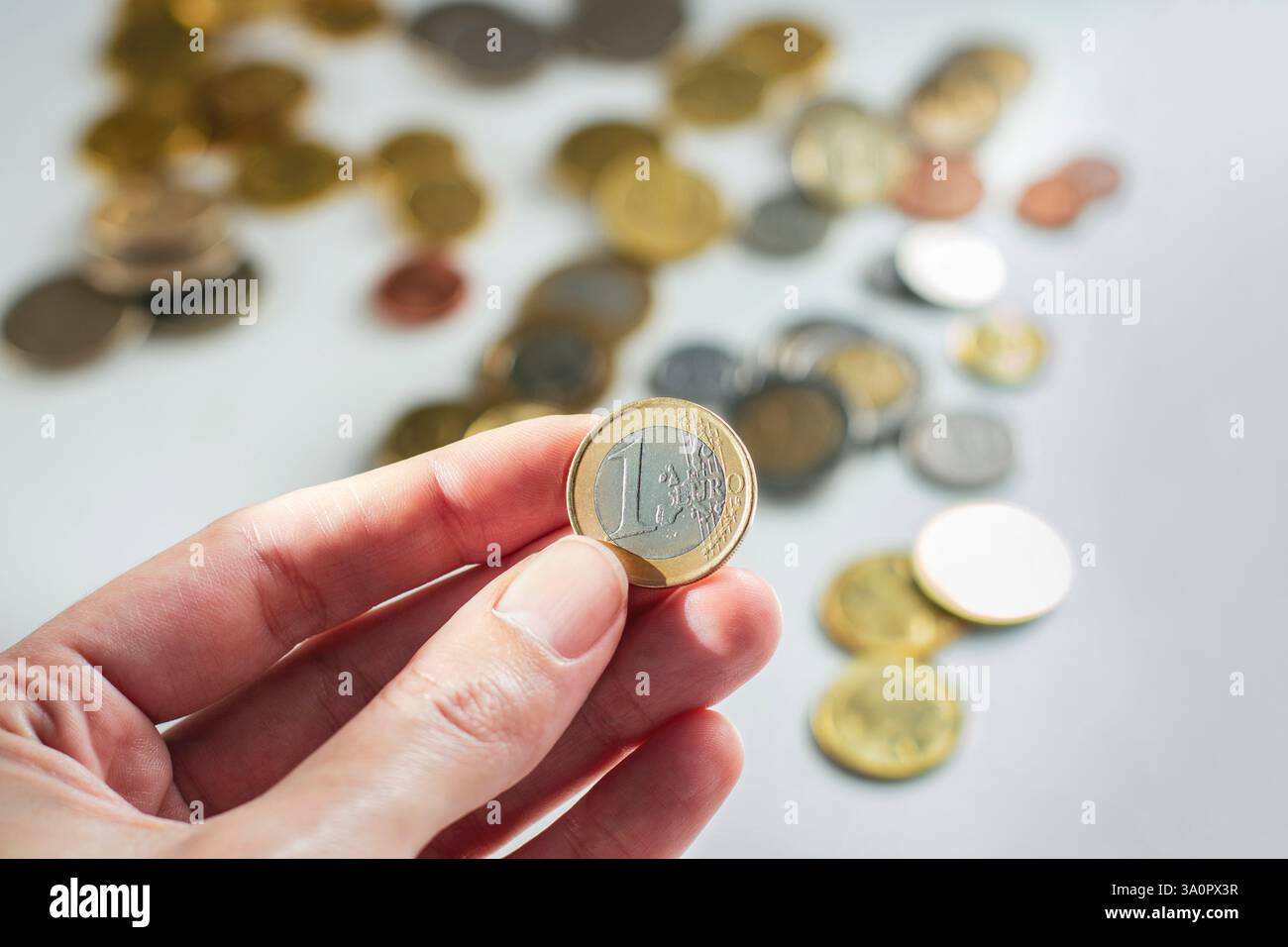 moneta da 1 euro in mano davanti a molte monete diverse sullo sfondo Foto Stock