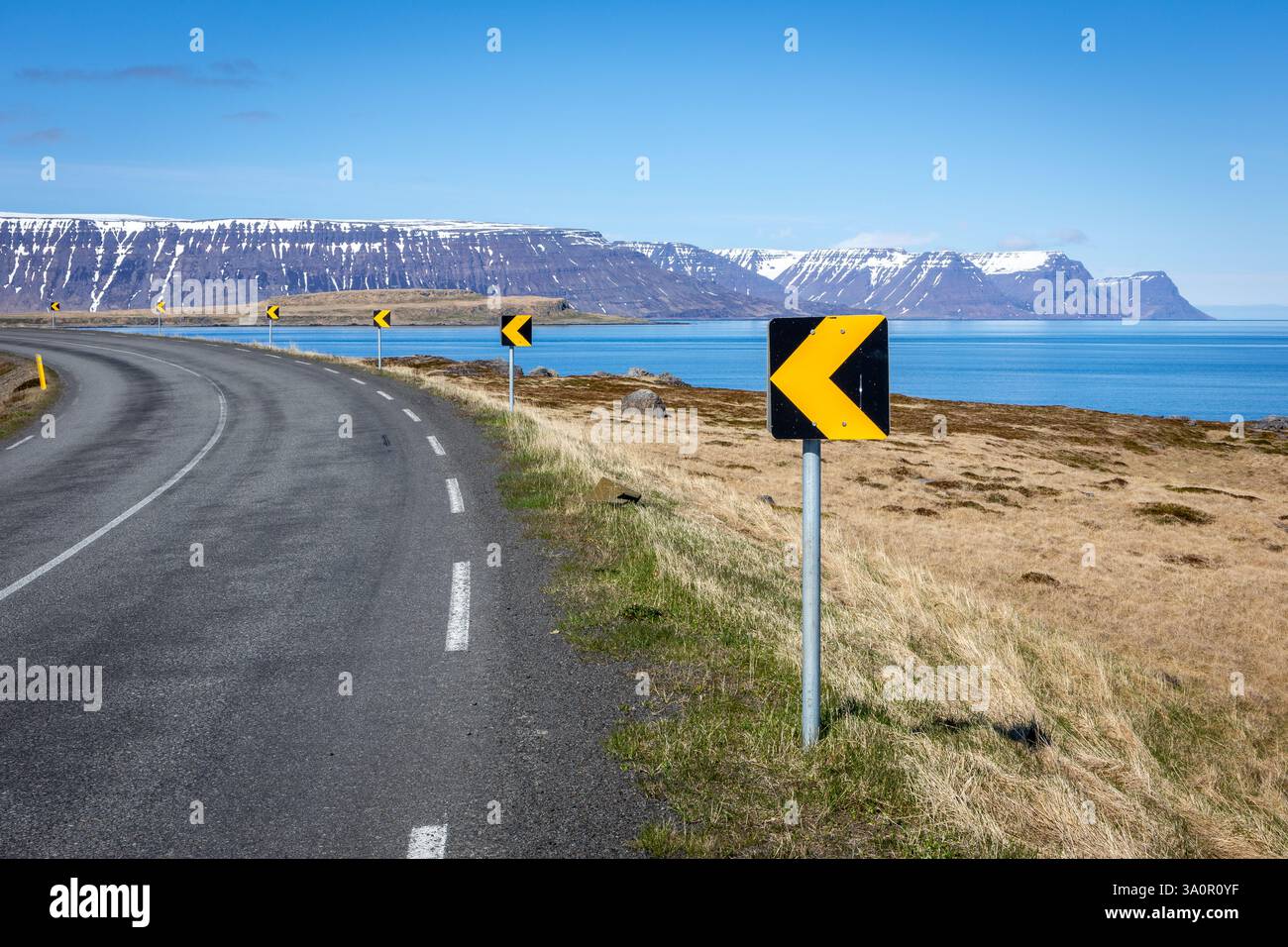 Tortuosa strada asfaltata attraverso i Westfjords in Islanda con montagne innevate e vista sul mare sullo sfondo. Foto Stock