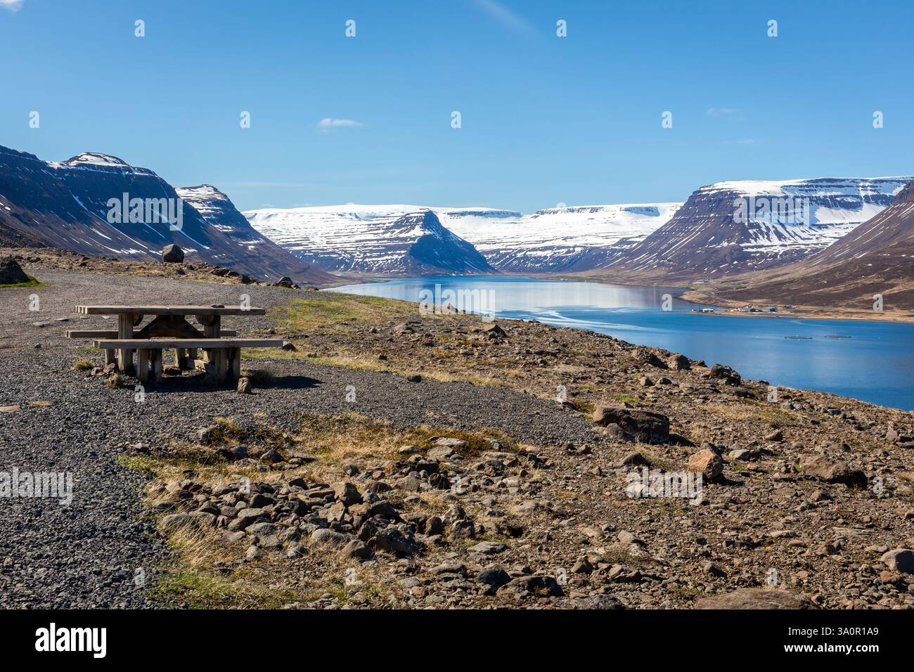 Tavolo da picnic in legno sulla riva di Isafjordur con montagne innevate e baia cristallina sullo sfondo, l'Islanda. Foto Stock