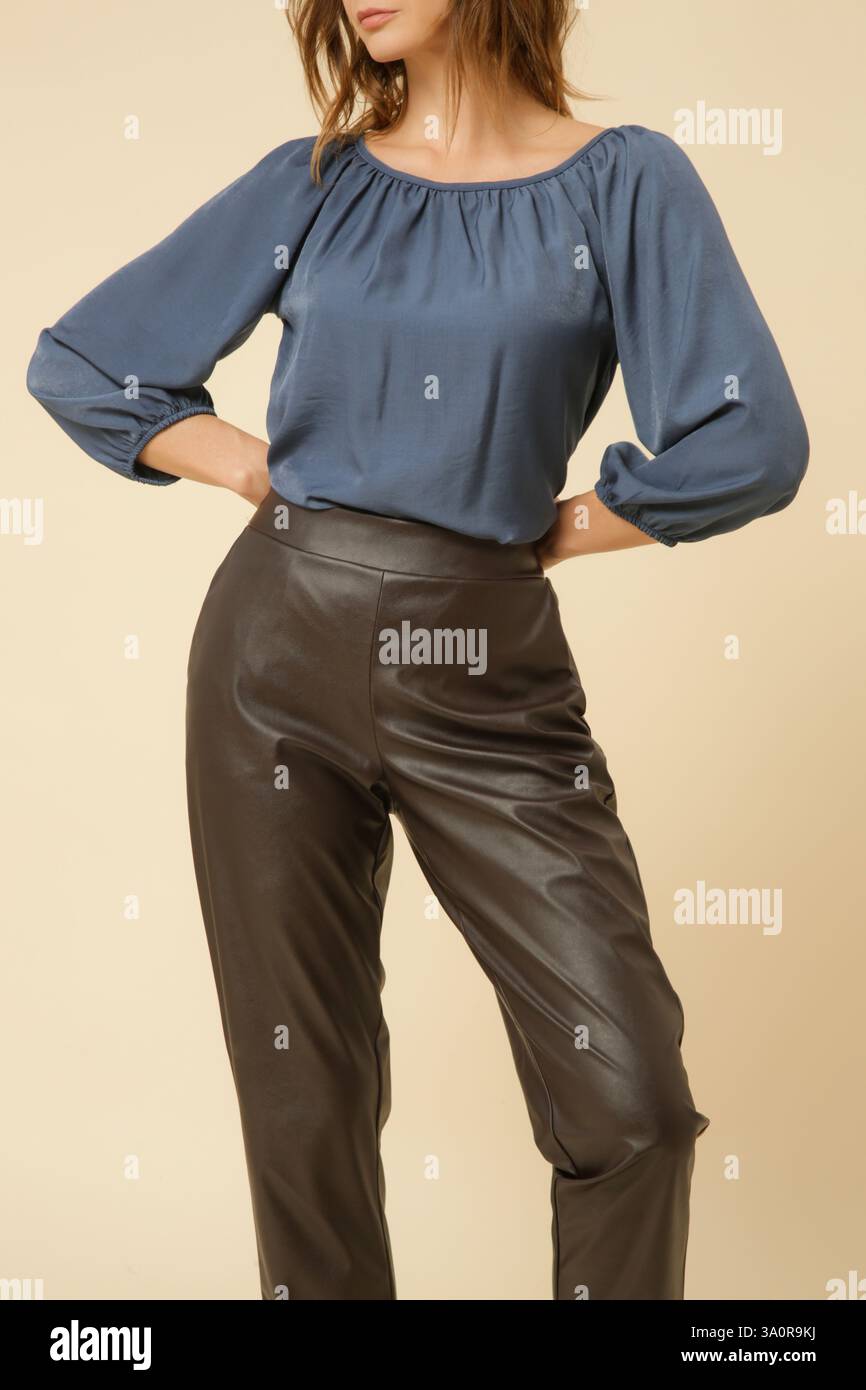 Fotografia in studio di una giovane modella donna che indossa una blusa blu e pantaloni neri in ecopelle. Collezione di moda autunnale invernale. Foto Stock