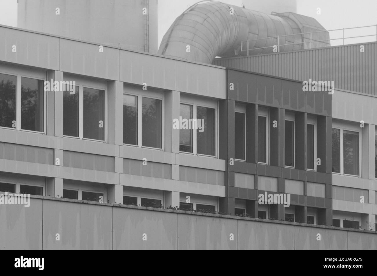 Tubo di ventilazione che avvolge le finestre di un ufficio di un edificio industriale in monocromia Foto Stock