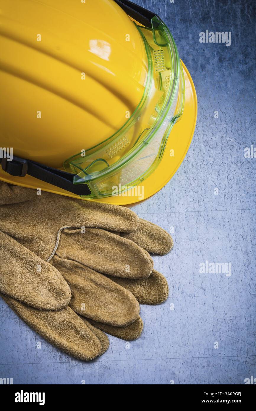 Composizione di guanti protettivi in pelle casco giallo da costruzione e occhiali di sicurezza trasparenti su fondo metallico graffiato concetto di costruzione Foto Stock
