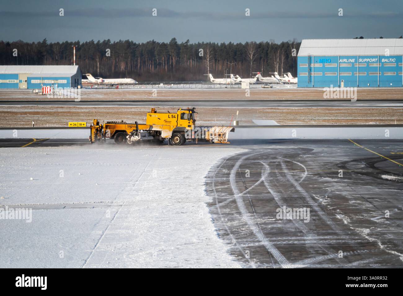 Riga, Lettonia - 15 febbraio 2025: I macchinari pesanti sgomberano la neve sulla pista dell'aeroporto internazionale di riga in inverno. Foto Stock