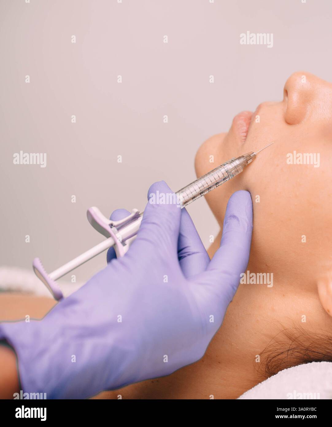 Un esperto cosmetologo sta iniettando con cura un trattamento viso nella guancia di un cliente in un ambiente spa pulito e contemporaneo. Foto Stock