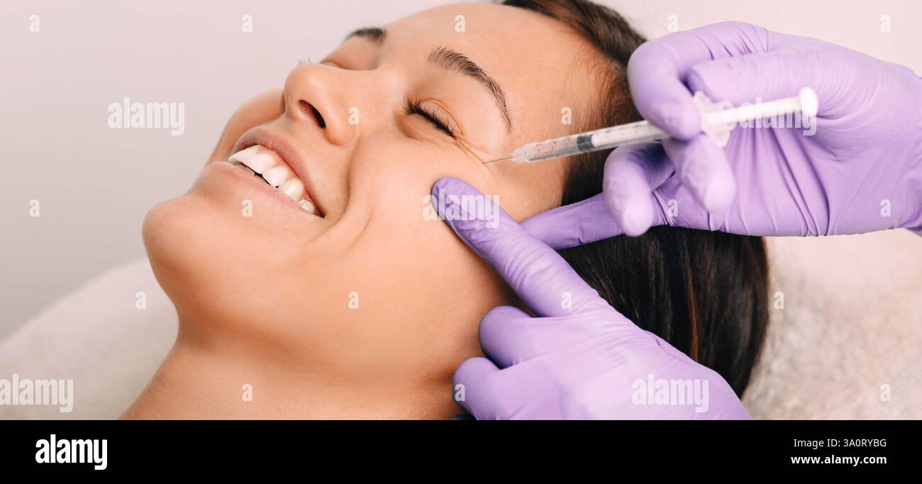 Un cliente ama una procedura cosmetica, in quanto un tecnico applica delicatamente il riempitivo, migliorando le sue caratteristiche naturali in un'atmosfera rilassante da salone. Foto Stock