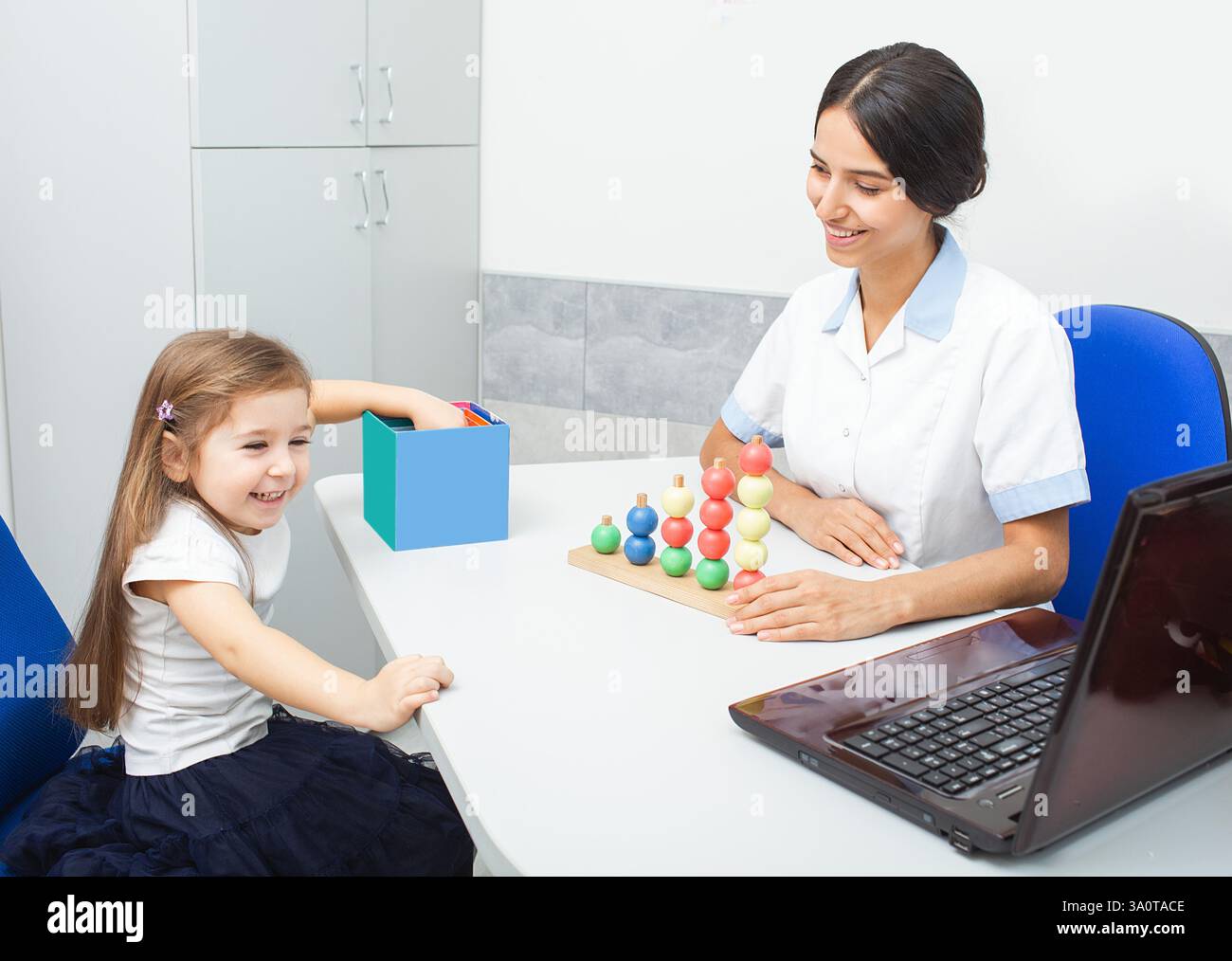 Un bambino si impegna con gioia con giocattoli colorati, mentre un terapista sul lavoro facilita lo sviluppo delle competenze attraverso il gioco in un centro terapeutico. Foto Stock