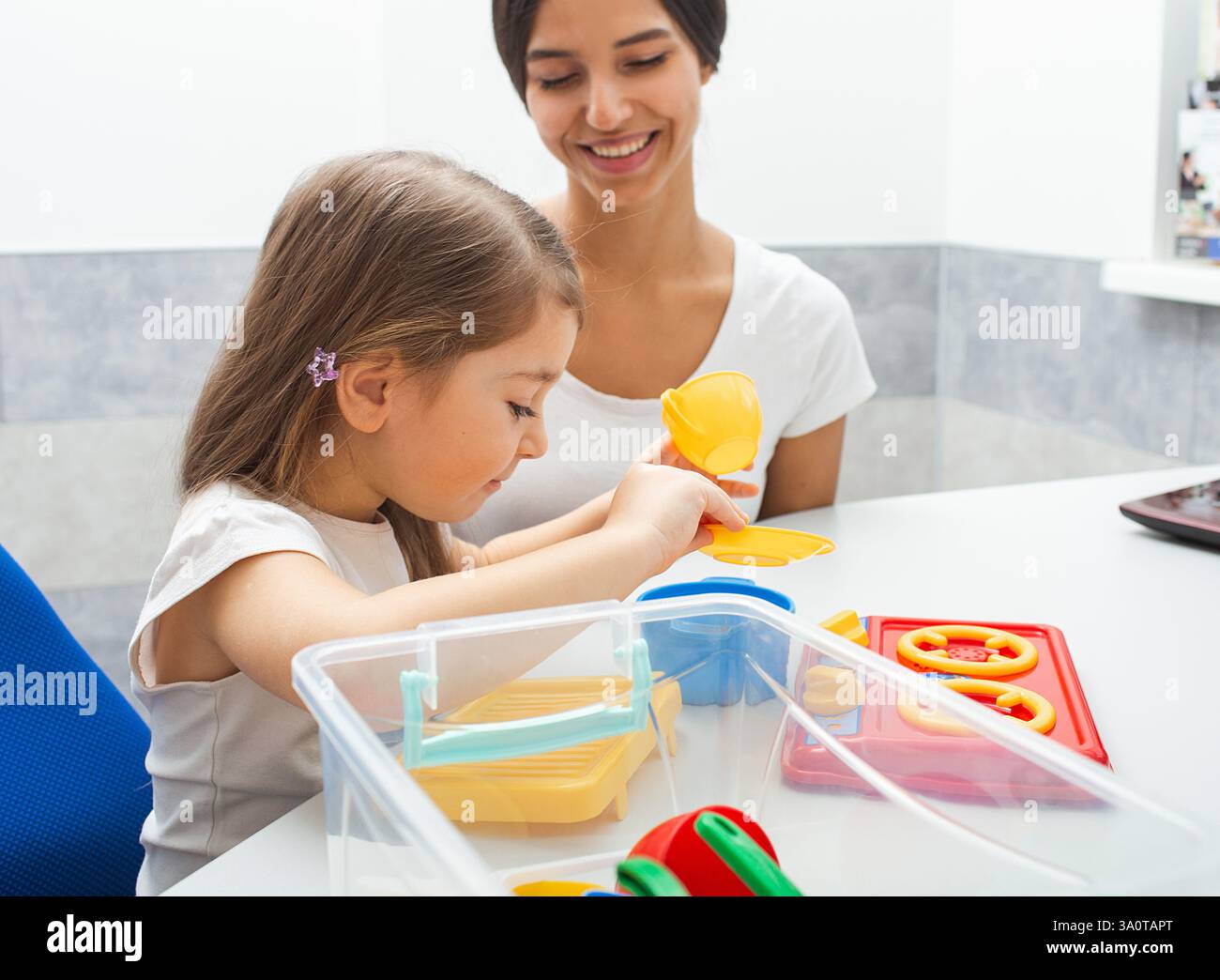 Il bambino si impegna in un'attività giocosa con un terapeuta, migliorando le capacità motorie e cognitive attraverso giocattoli colorati in un ambiente terapeutico. Foto Stock