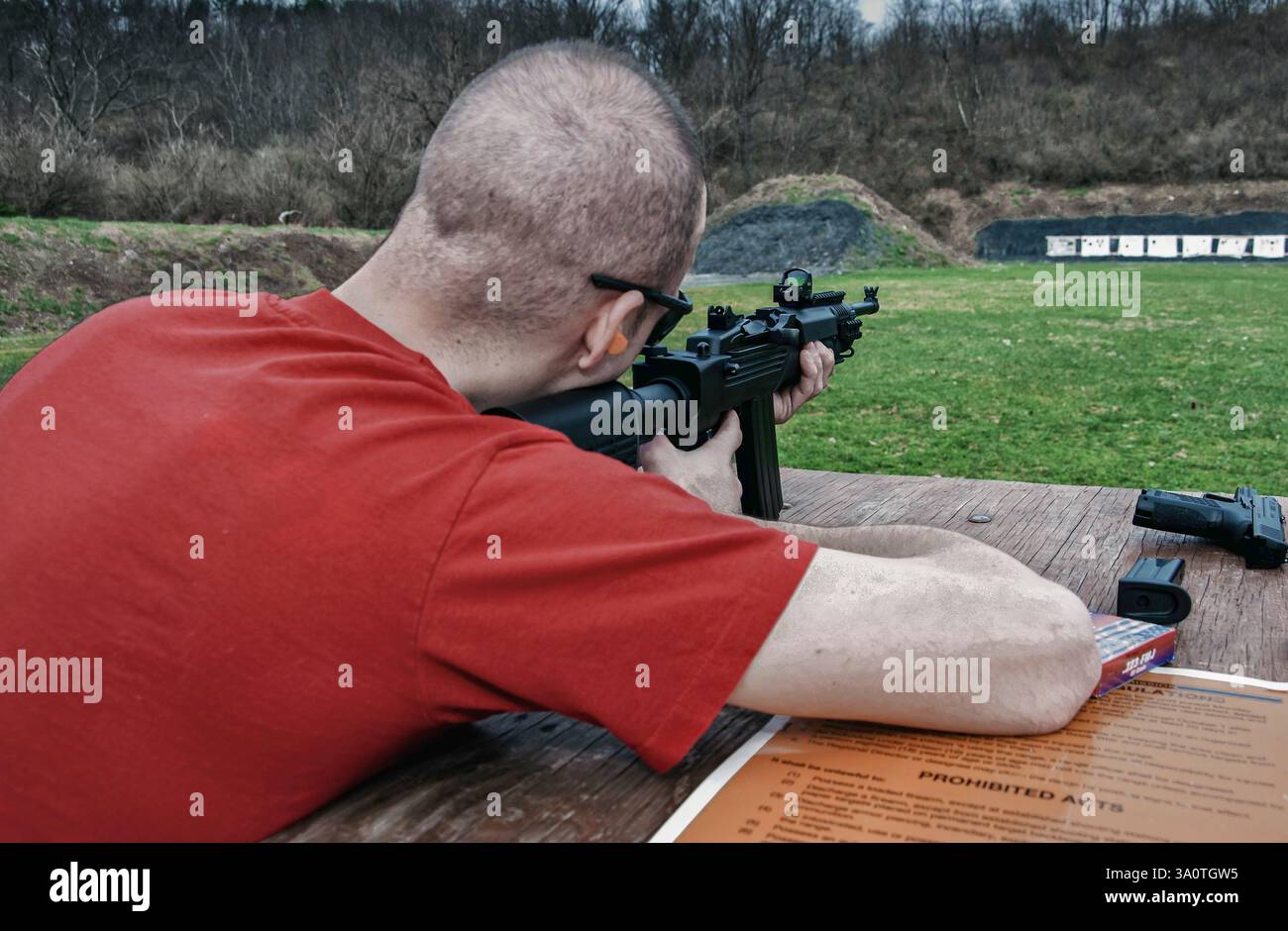 Uomo che spara un'arma d'assalto al raggio di tiro contro bersagli di carta Foto Stock