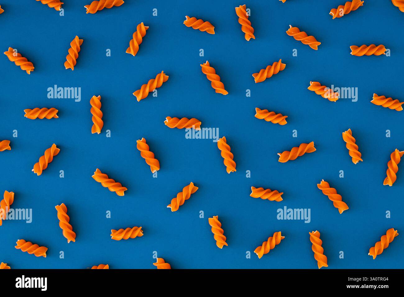 Fantasia gastronomica alla moda fatta di pasta fusilli di colore arancione naturale su sfondo blu. Concetto minimale. L'estetica della pasta. Disposizione piatta, vista dall'alto. Foto Stock