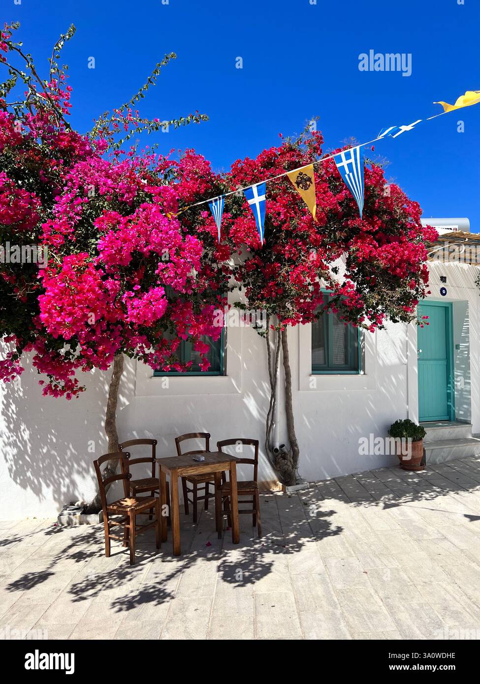 Un affascinante cortile greco con cieli blu, vibrante bougainville e posti a sedere rustici Foto Stock