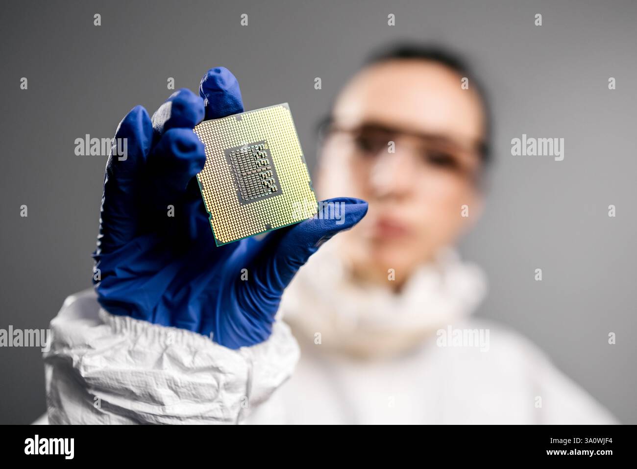 In una fabbrica di elettronica high-tech, un progettista con una tuta sterile esamina un microchip con guanti, perfetto per mostrare l'innovazione Foto Stock