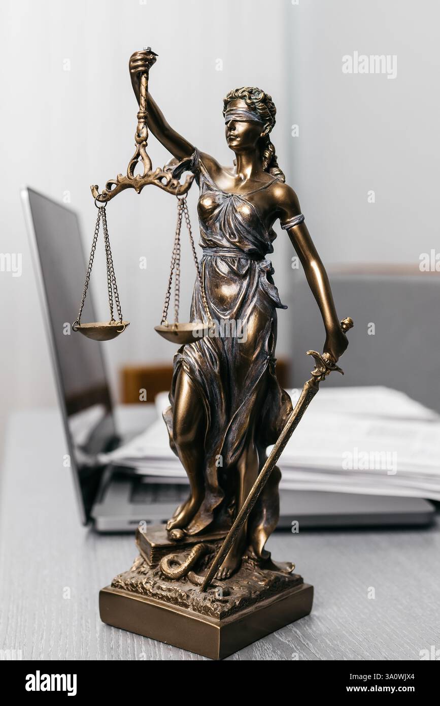 Una scrivania da avvocato con documenti contrattuali, un portatile e una statua della dea della giustizia. Un simbolo della legge, dei servizi legali e della giustizia Foto Stock