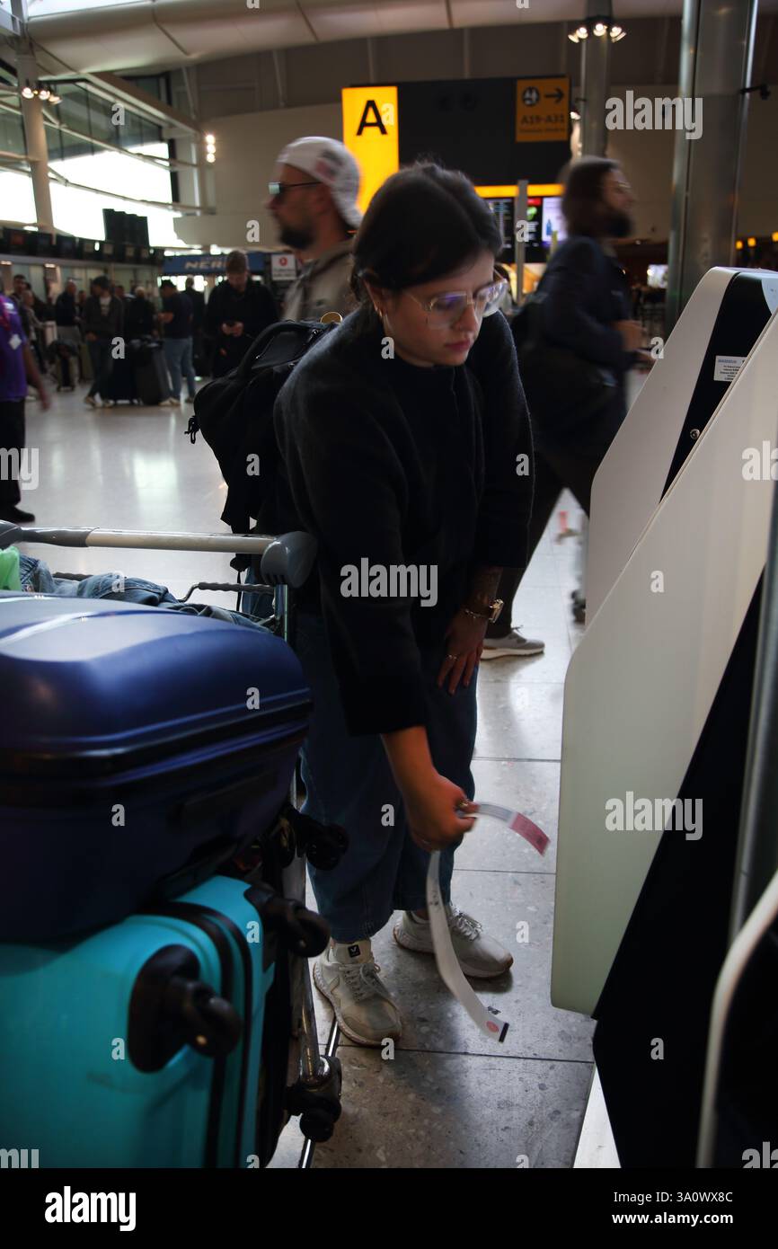 Donna che utilizza il check-in automatico e stampa l'etichetta della valigetta presso l'aeroporto di Londra Heathrow, Inghilterra Foto Stock