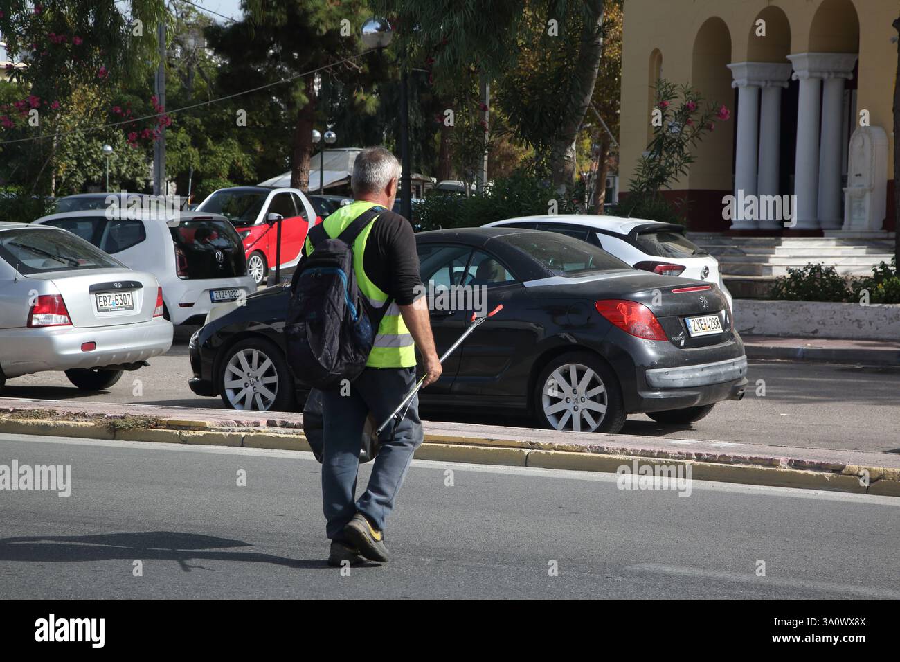 Raccolta rifiuti con raccoglitrice di rifiuti e giubbotto ad alta visibilità che attraversa la strada Voula Atene Attica Grecia Foto Stock