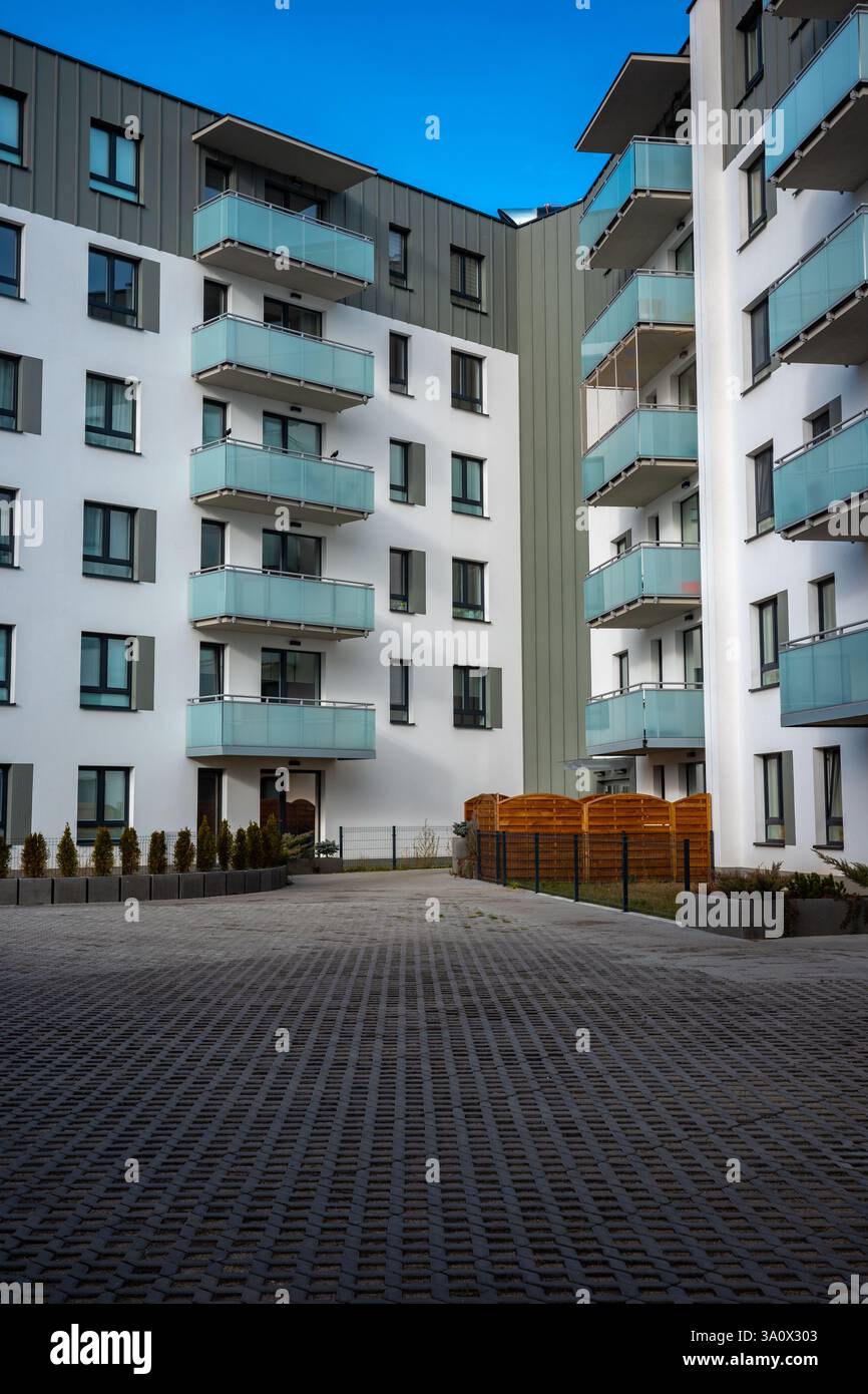 La facciata di un moderno edificio di appartamenti di colore grigio chiaro si affaccia sul cielo blu. Gli appartamenti sono dotati di balconi smaltati. Foto Stock