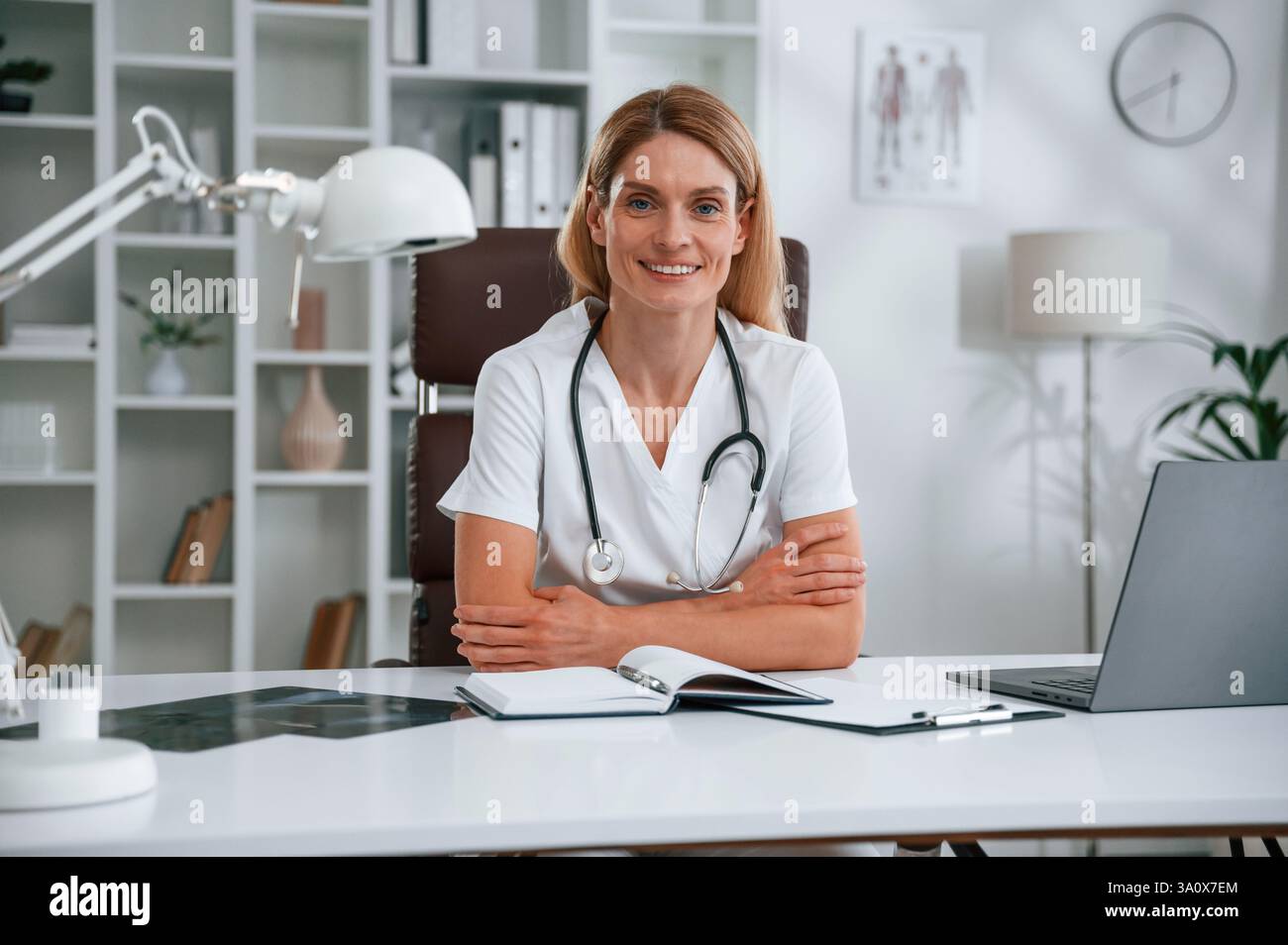 Seduti accanto al tavolo. Giovane medico donna in camice bianco è al chiuso. Foto Stock