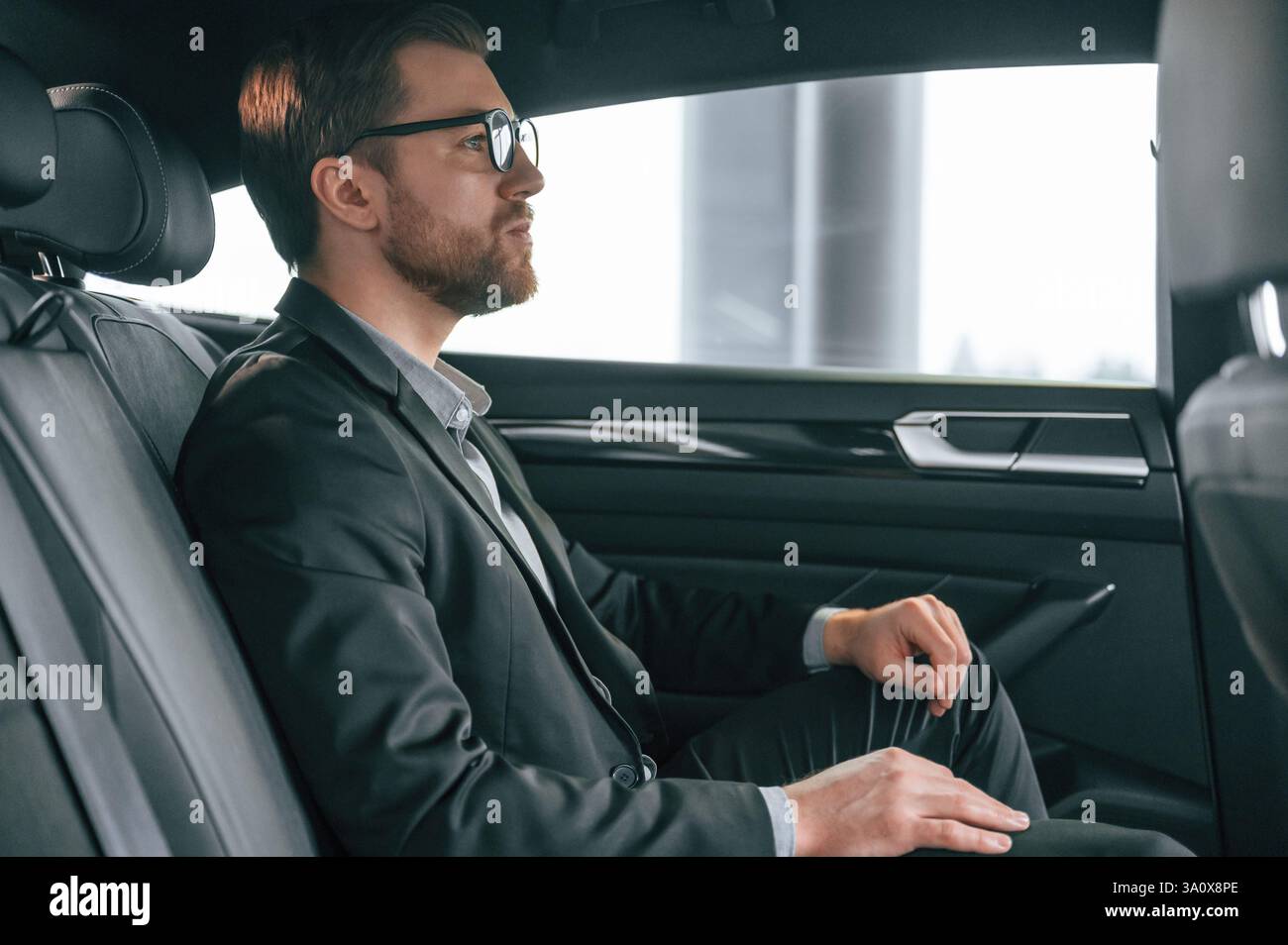 L'uomo in abiti da lavoro formali è seduto nell'automobile moderna. Foto Stock