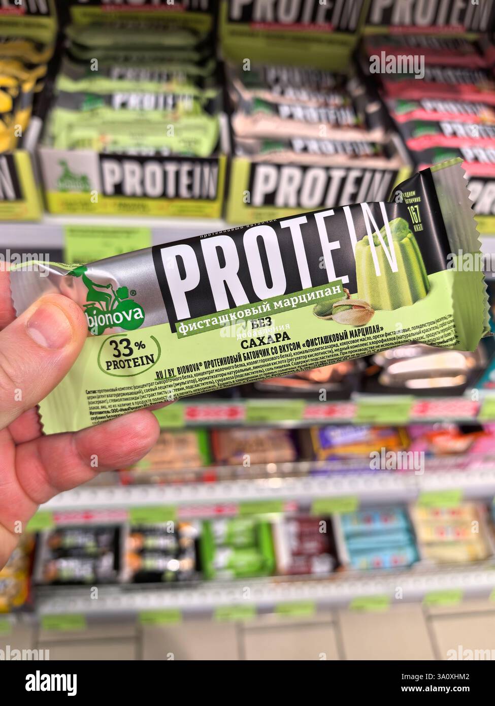 Bobruisk, Bielorussia - 22 febbraio 2025: Un acquirente tiene una barretta di proteine in un corridoio di alimentari pieno di opzioni di spuntini colorati. La barra evidenzia il dado Foto Stock