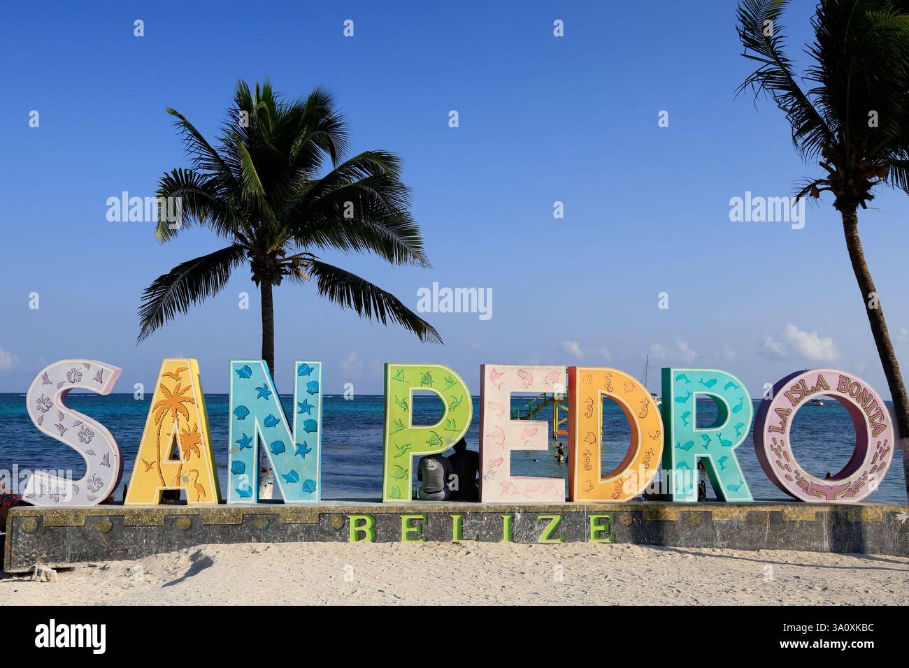 Colorato cartello di San Pedro con palme vicino alla spiaggia pubblica nel centro della città con il Mar dei Caraibi sullo sfondo. San Pedro. Ambergris Caye. Belize Foto Stock