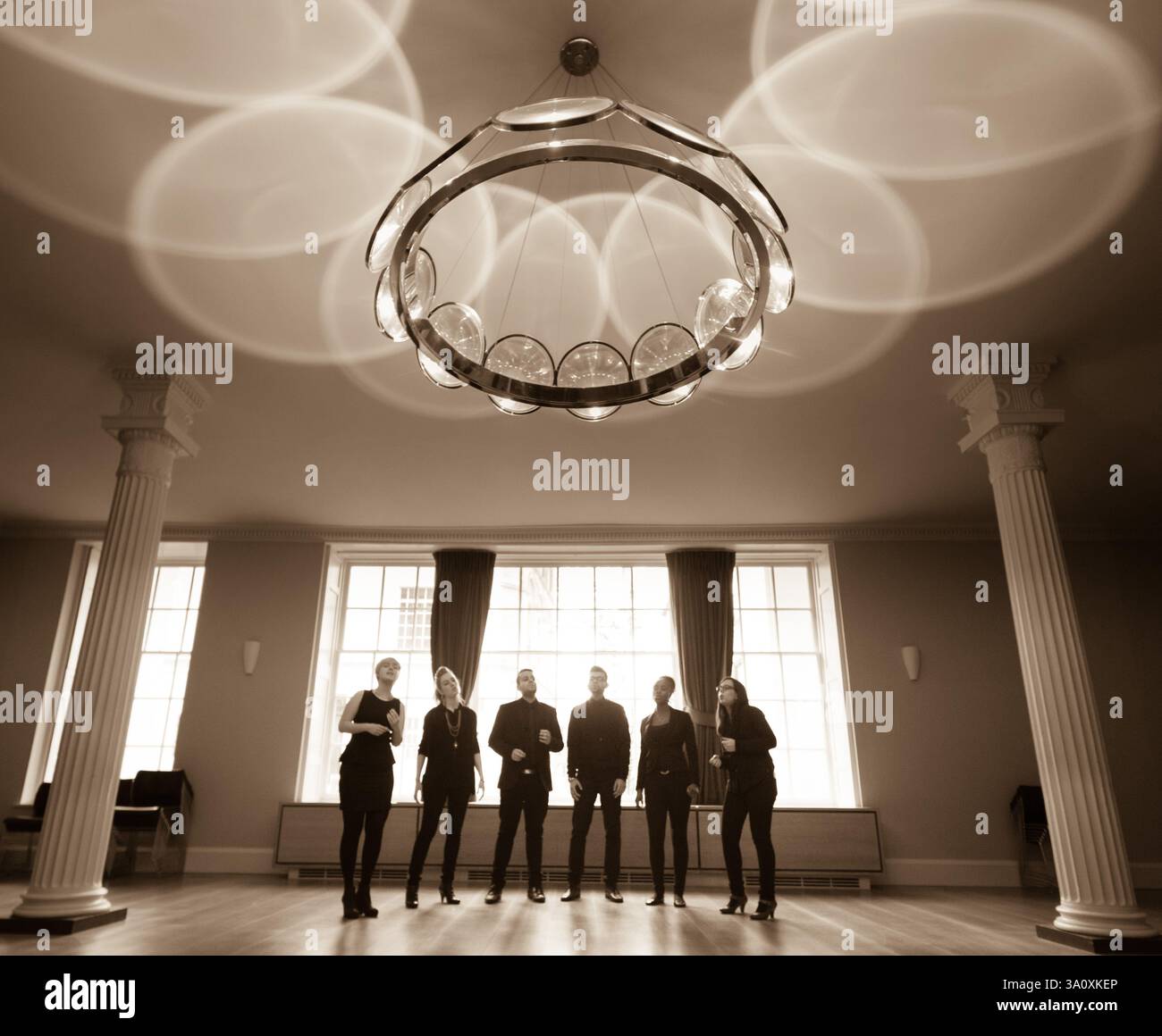 Il gruppo canta nella grande sala della RSA. Finestre e colonne di grandi dimensioni sono visibili. Foto Stock