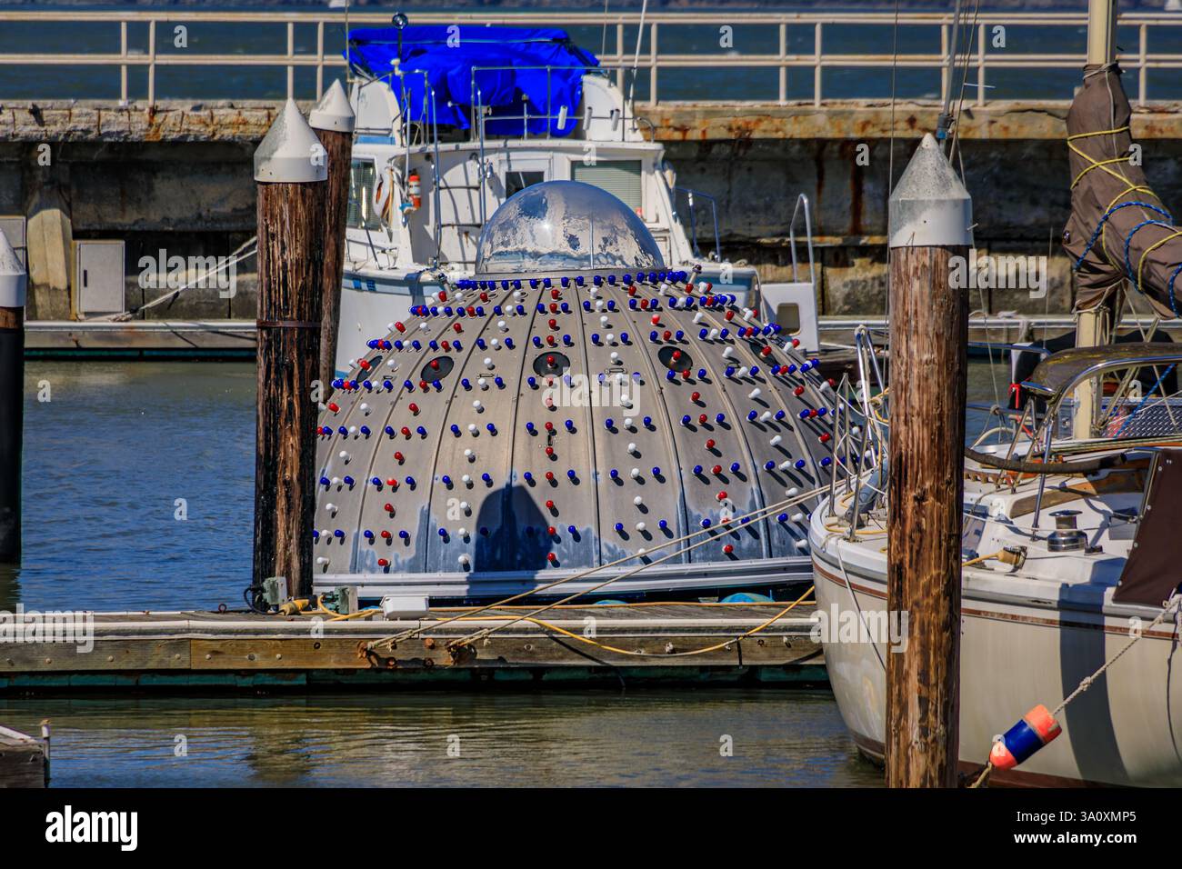 Una barca ormeggiata nel porticciolo di San Francisco con aspetto simile a un UFO, forma a cupola con luci blu e rosse sulla superficie che si riflettono nell'acqua Foto Stock