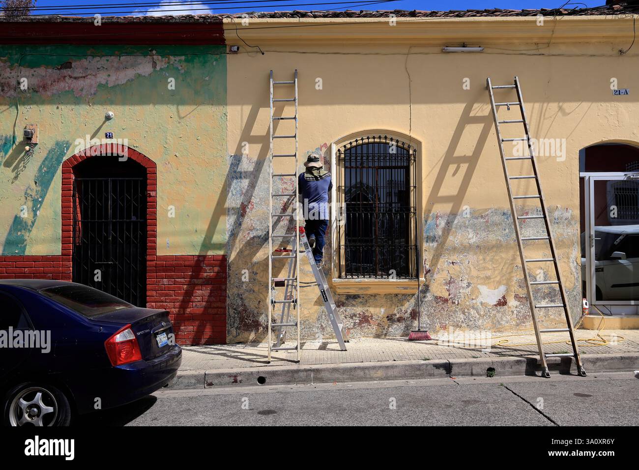 Un lavoratore su una scala che ripara il muro esterno di una casa in stile coloniale sulla strada di Santa Ana. El Salvador Foto Stock