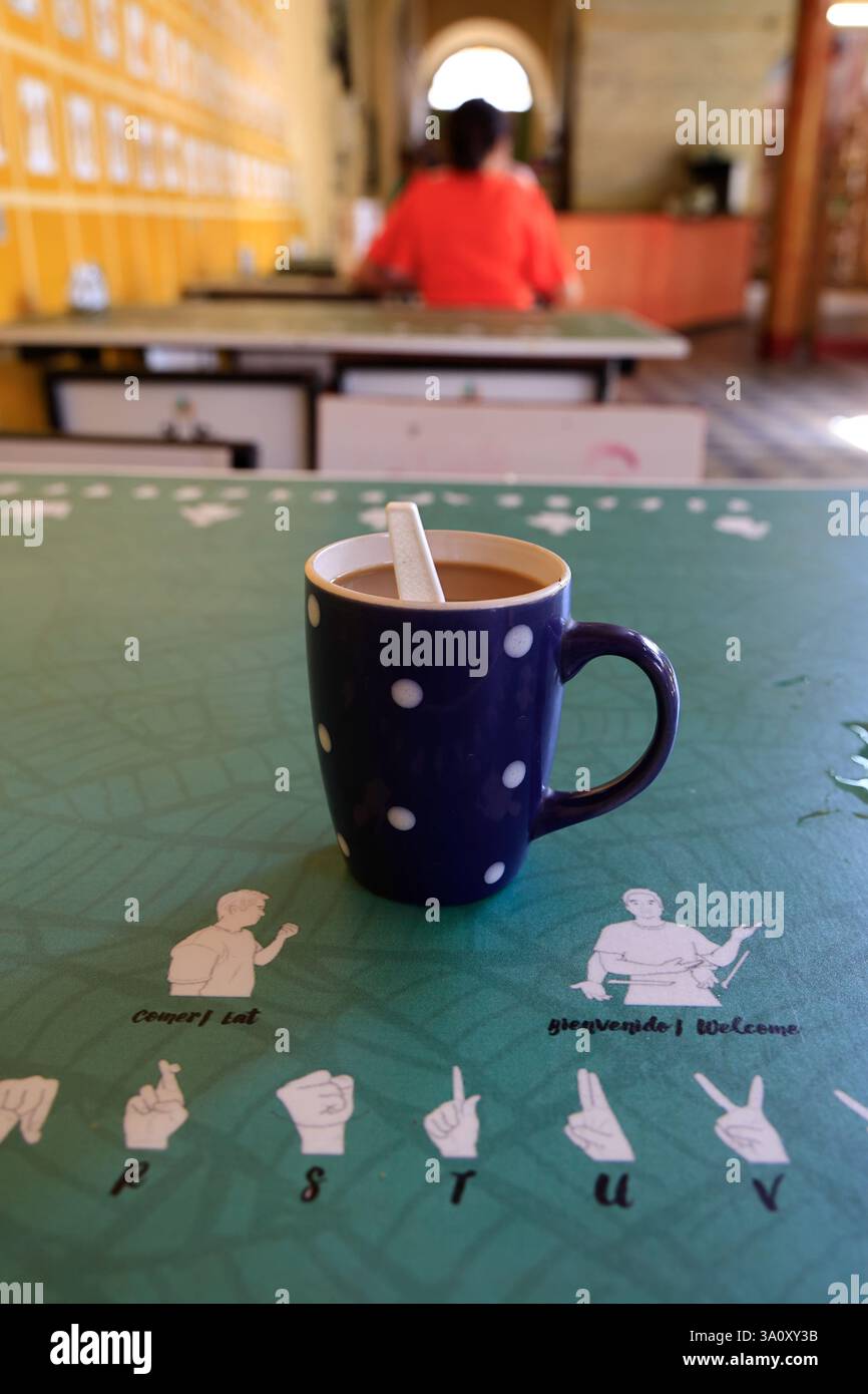 Una tazza di caffè sul tavolo del Cafe de la Sonrisas (caffè sorridente) con figure di linguaggio dei segni. Questo caffè occupa solo persone sorde-muti e disabili nel centro storico di Granada. Nicaragua Foto Stock