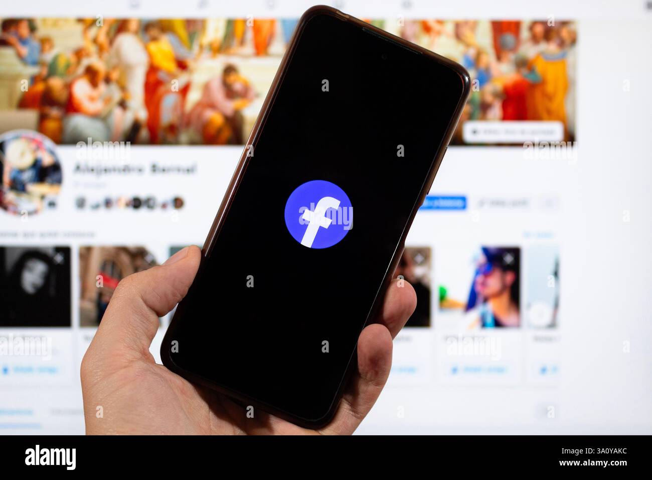 BOGOTÀ, COLOMBIA - 05 MARZO 2025 una mano destra maschile con il simbolo dei social media di facebook all'interno di uno smartphone con l'interfaccia facebook sullo sfondo Foto Stock